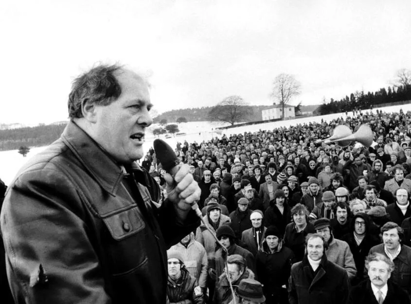British Leyland union leader Derek Robinson speaking into a microphone before a mass meeting of striking workers.