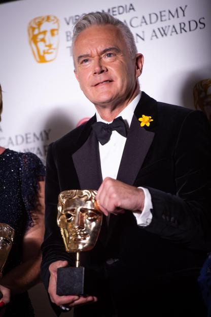 Huw Edwards holding a BAFTA award.