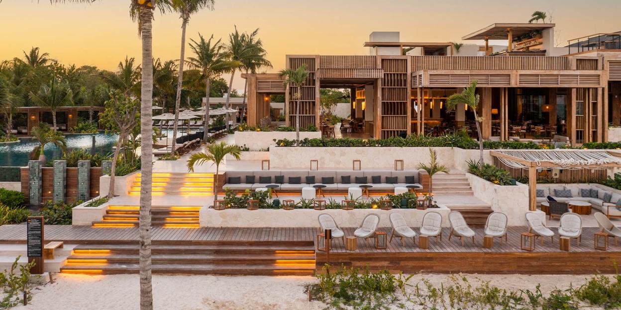 Fairmont Mayakoba luxury hotel at sunset, with a pool, multiple decks, and wooden buildings.