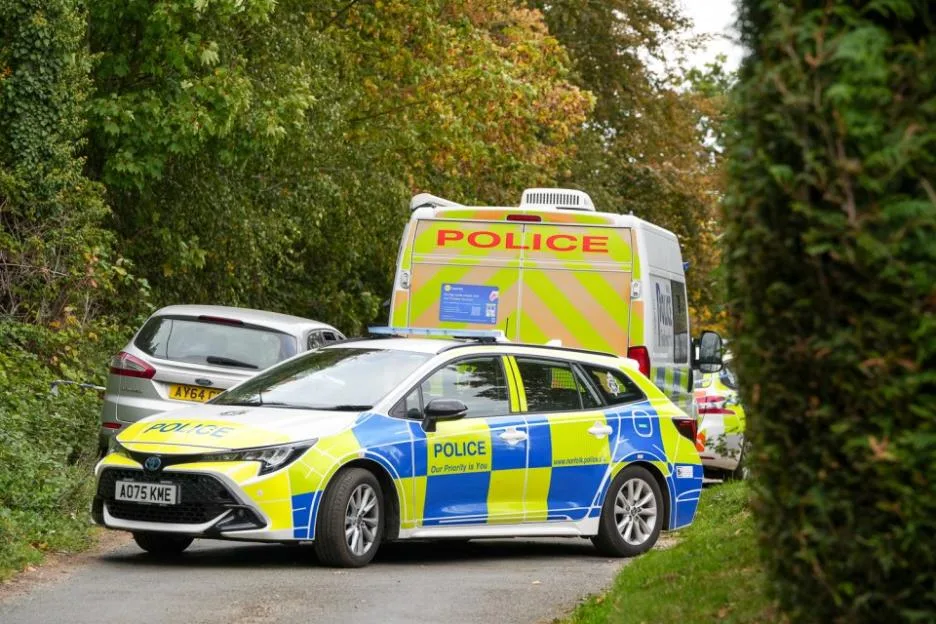 Police vehicles parked on a road at the scene of an investigation.