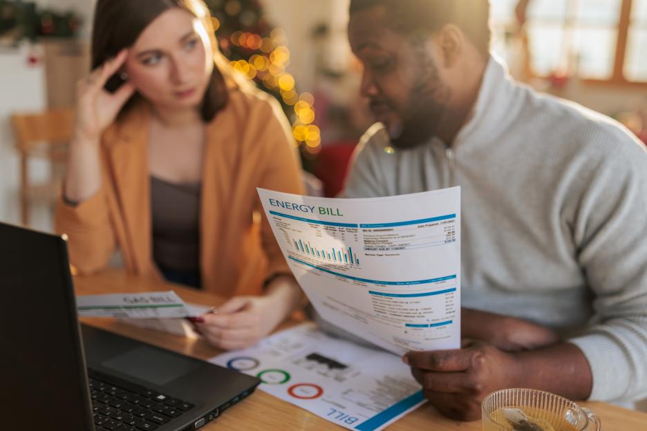A worried couple examining an energy bill and other financial documents at home.