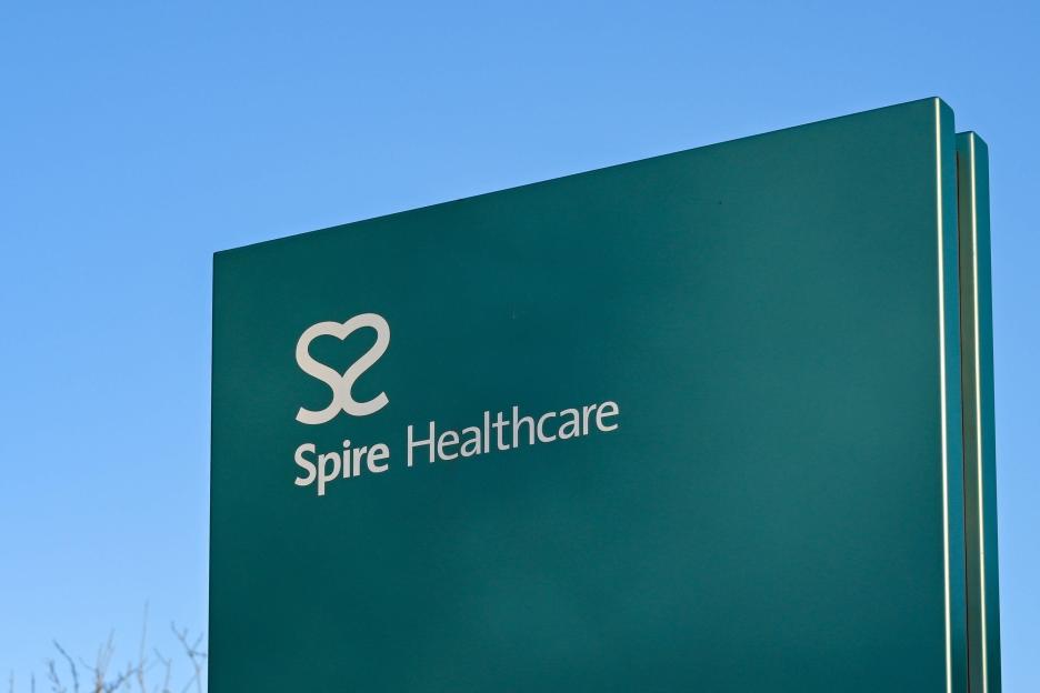 Close-up of a teal Spire Healthcare sign against a blue sky.
