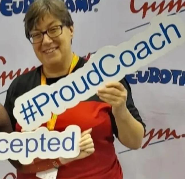 Justine Leader smiling and holding a sign that says "#ProudCoach".