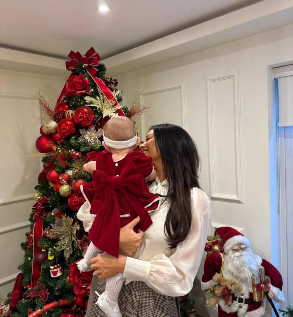 Michelle Keegan holding baby Palma in front of a Christmas tree and a Santa Claus figurine.