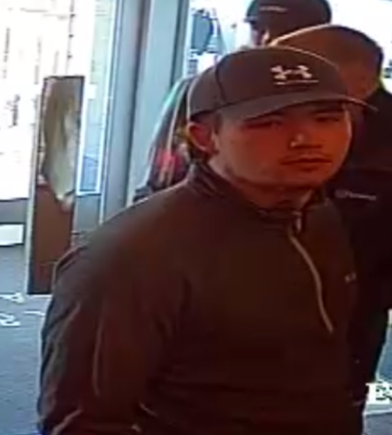 CCTV image of a man wearing a dark baseball cap with a white logo and a dark long-sleeved shirt with a zipper.