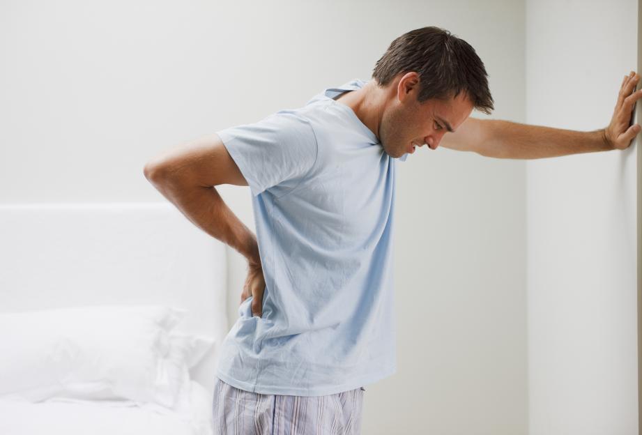 Man experiencing back pain leaning against a wall