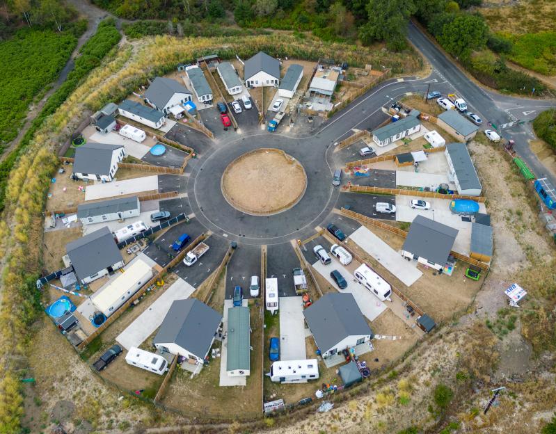 Aerial view of a circular residential development with houses and numerous caravans, some with small swimming pools and trampolines.