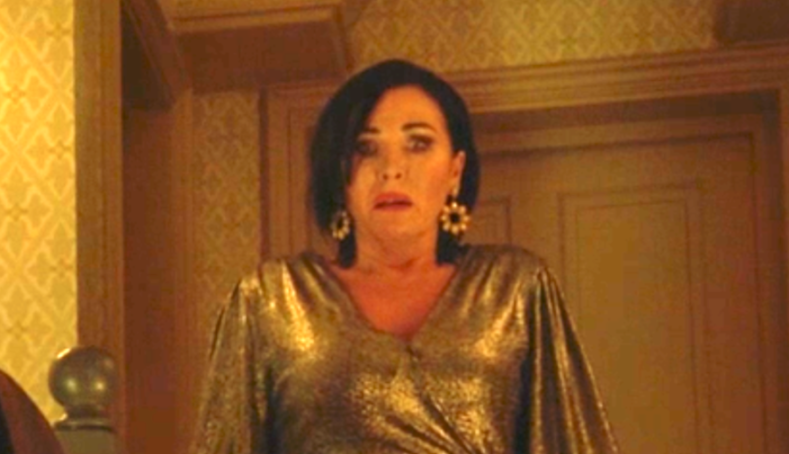 A woman with dark hair and a gold dress looking shocked.