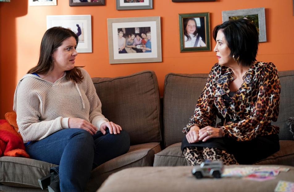 Two women sit on separate couches, facing each other in conversation.