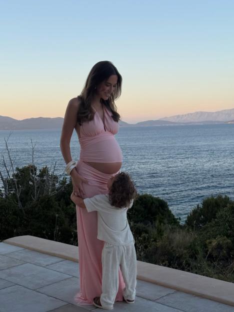 Pregnant Lucy Watson showing her baby bump while a child hugs her waist.