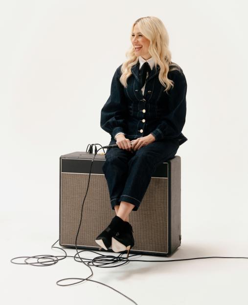 Pixie Lott sitting on a speaker with a microphone in her hands.