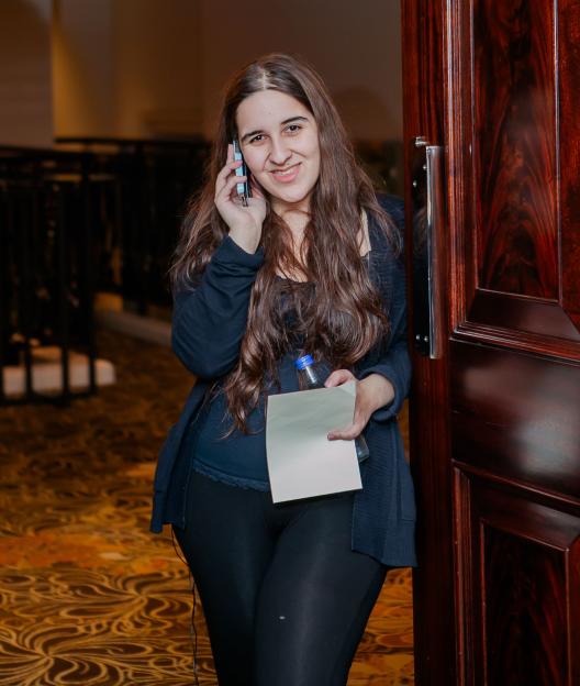 Megan Bhari holding a bottle, paper, and talking on a cell phone.
