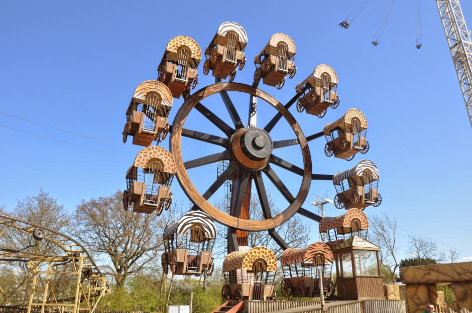 Ferris wheel ride at Flamingo Land, with animal-print covered wagon gondolas against a clear blue sky.