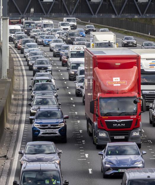 Heavy traffic on the M25 in Egham, UK, with a red Royal Mail truck in the foreground.