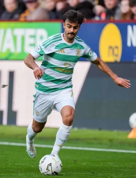 A Celtic player in a green and white hooped jersey dribbles the ball past a Motherwell player during a Scottish Premiership match at Fir Park.
