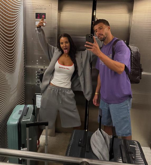 Maya Jama and Ruben Dias pose for a selfie in an elevator, with suitcases on the floor.