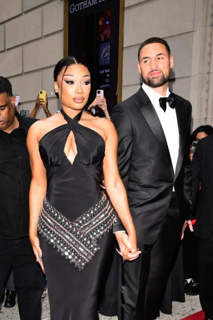 Megan Thee Stallion in a black halter-neck gown with a beaded waistline holds hands with Klay Thompson in a tuxedo.