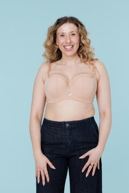 Woman in a nude bra and dark jeans smiling at the camera.