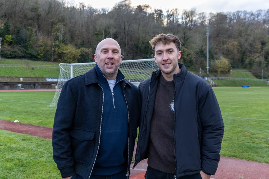Two men standing on a track next to a soccer field.