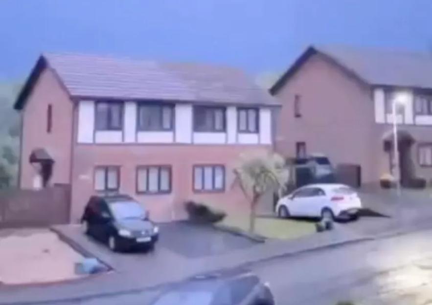 A purple sky above two houses with cars in their driveways, depicting the lightning strike that set a house ablaze.