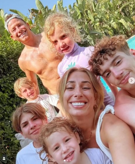 A family of seven smiles for a selfie outdoors.