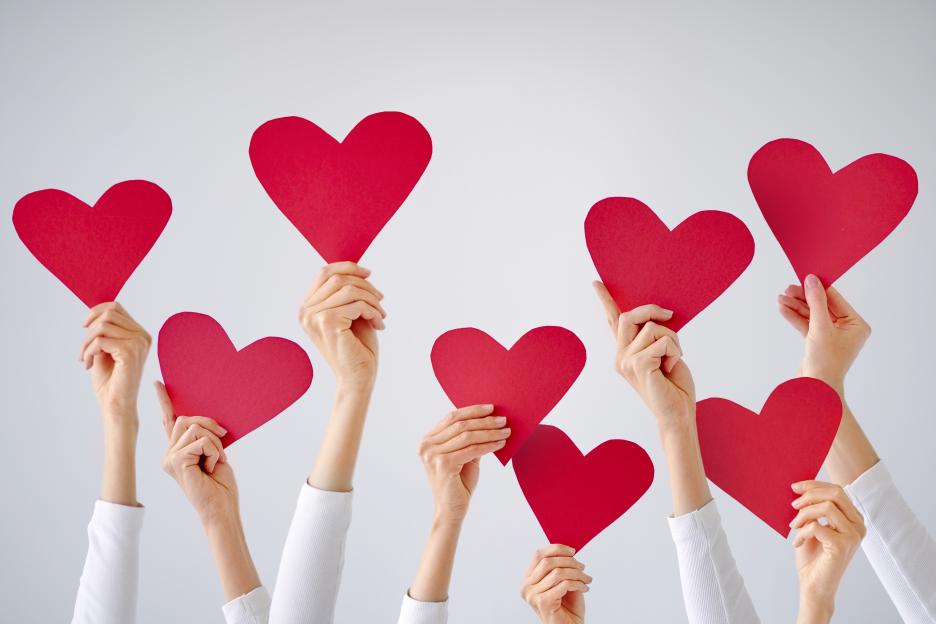 Many female hands holding red paper hearts.