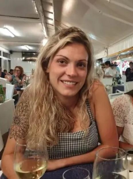 A woman with curly blonde hair and a tattoo on her shoulder smiling at a restaurant.