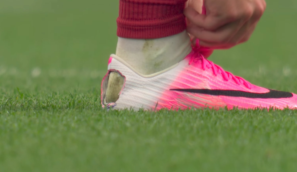 Player tying the laces of a pink Nike soccer cleat with a torn heel.