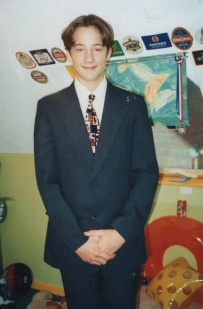 A young man in a dark suit and patterned tie smiling at the camera.