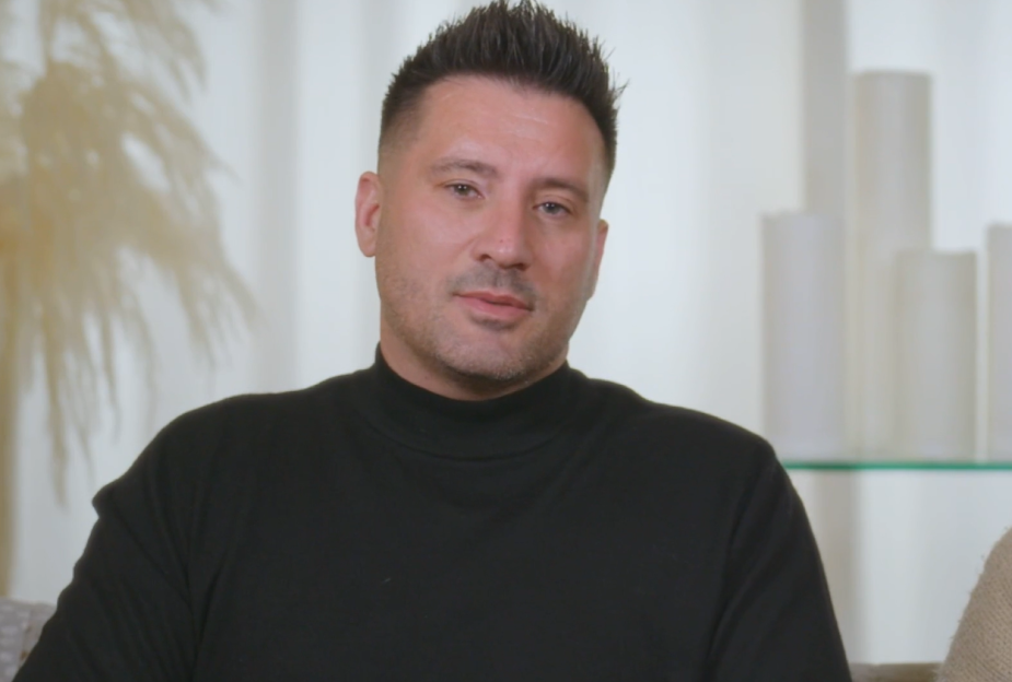 A man with a spiked haircut and black turtleneck looks at the camera.