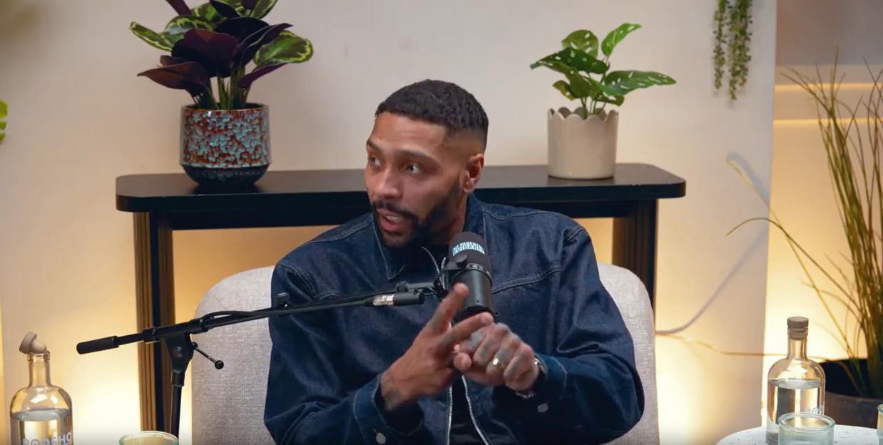 A man in a denim jacket talking into a microphone during a podcast.