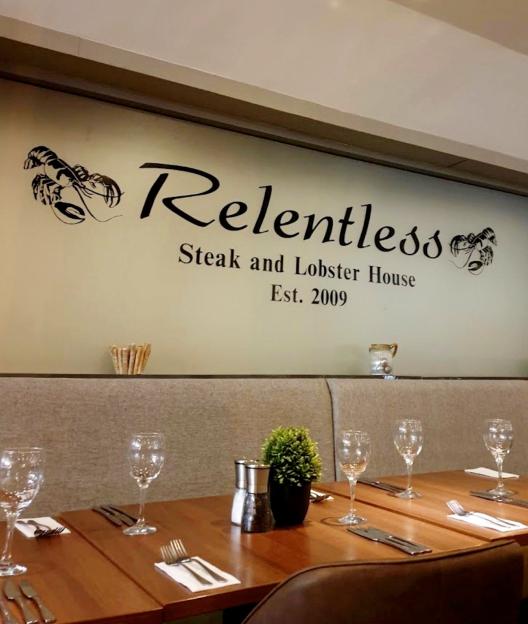 Interior of Relentless Steak and Lobster House restaurant with logo on the wall.