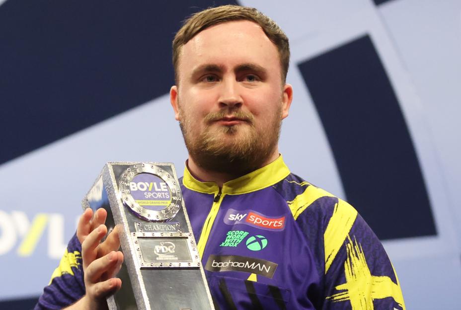 Luke Littler holding the Boyle Sports World Grand Prix trophy.