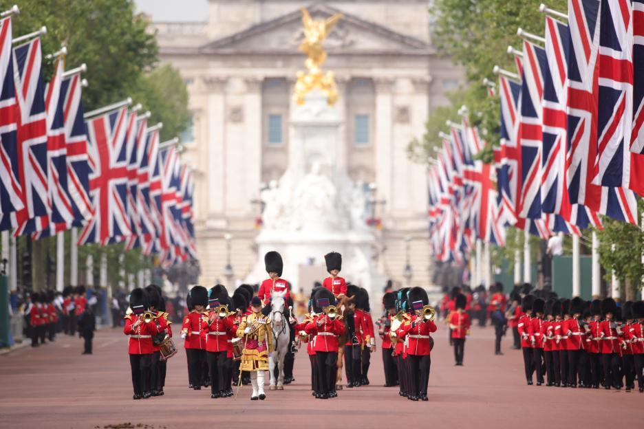 The Band of The Irish Guards march down The Mall during the Trooping the Colour ceremony, with Buckingham Palace and Union Jack flags in the background.