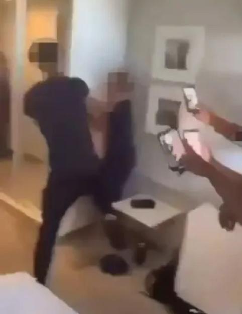 Two young men fighting in a room, with others recording on phones.