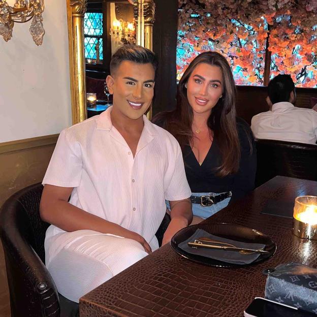 Junaid Ahmed and Lauren Goodger sitting at a table with a lit candle and a plate of cutlery.