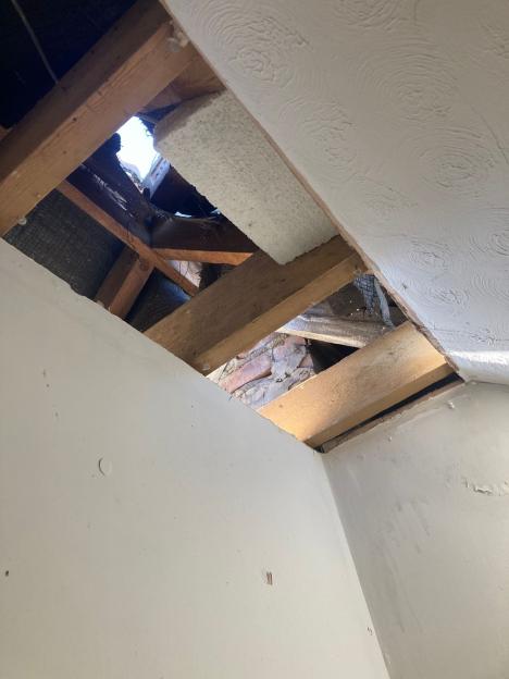 Damaged roof with a large hole and exposed wooden beams.