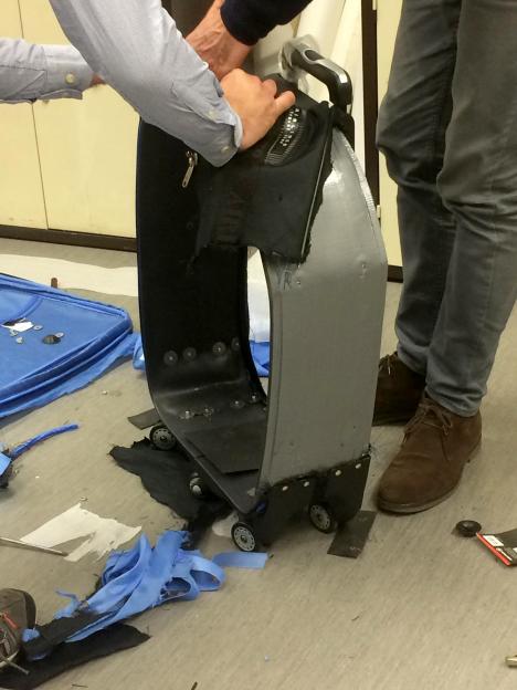 Police taking apart a suitcase to reveal hidden drugs.