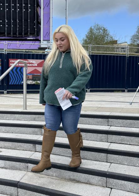 Hannah Bloor walking on steps outside, holding a paper and marker.