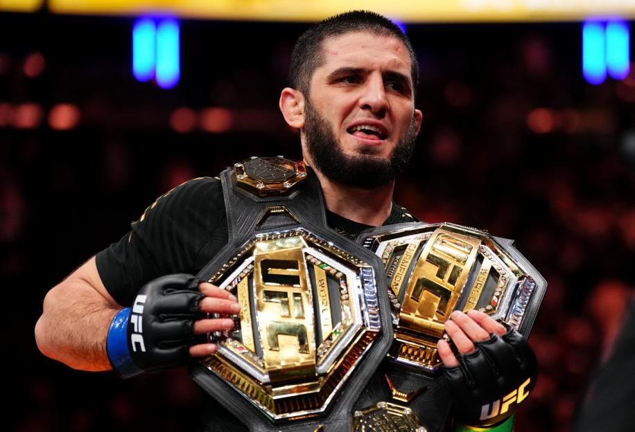 Islam Makhachev holding two UFC championship belts.