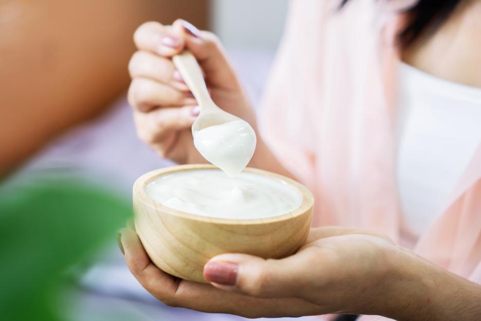 A woman is holding a wooden bowl of yogurt with a spoon in it