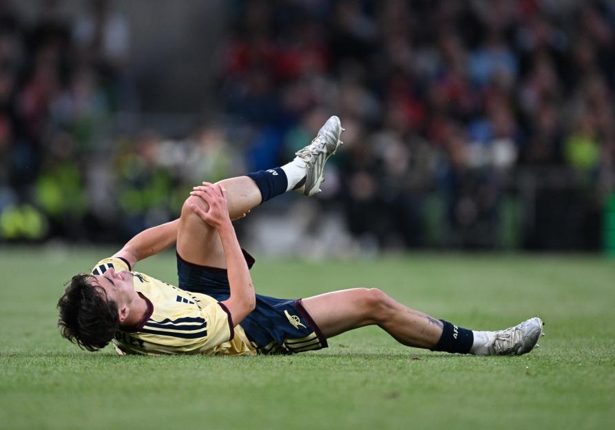 Louie Copley of Arsenal FC injured on the grass, holding his leg.