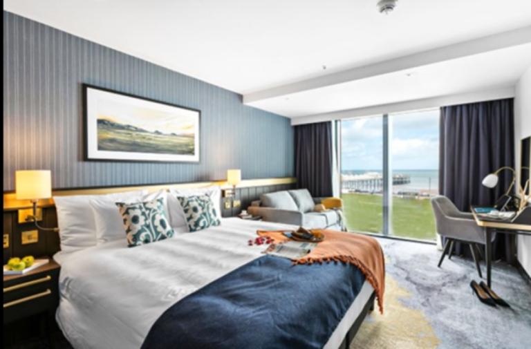 A hotel room at Mercure Paignton Hotel with a bed, desk, and view of the sea and pier.