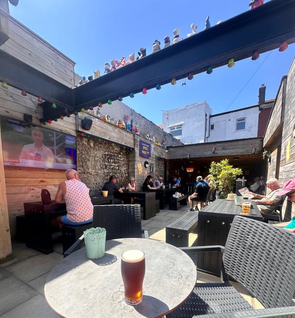 A beer on a table in an outdoor pub garden with people sitting at other tables.