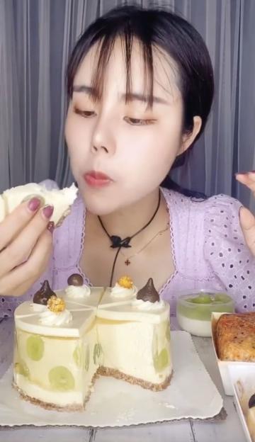 A woman with dark hair and bangs eating a slice of cheesecake with grapes inside.