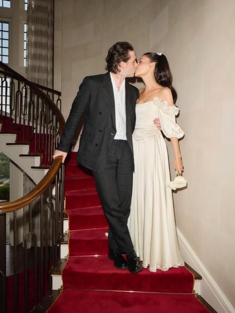 Brooklyn Beckham and Nicola Peltz kissing on a red carpeted staircase.
