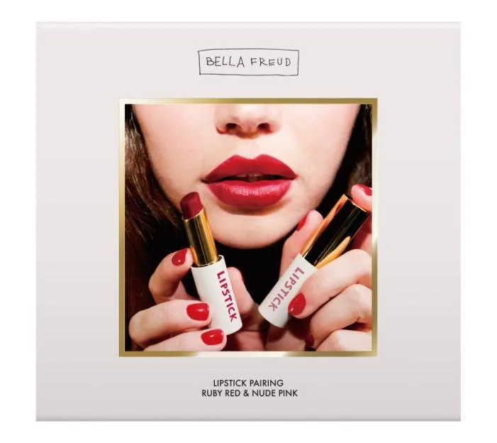 Close-up of a woman's mouth with red lipstick, holding two tubes of "Bella Freud" lipstick.
