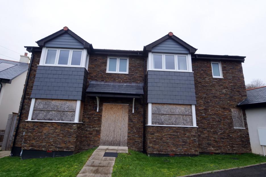 An abandoned new-build home with boarded-up windows and door.