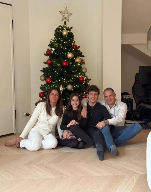 Family of four sitting on a wooden floor in front of a decorated Christmas tree.