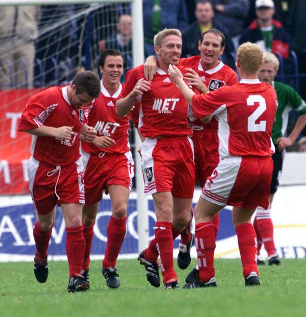 A group of five male football players in red and white uniforms celebrating a goal.